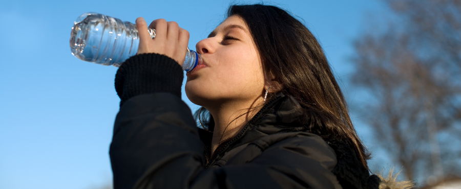 Mulher bebendo água no frio para se hidratar